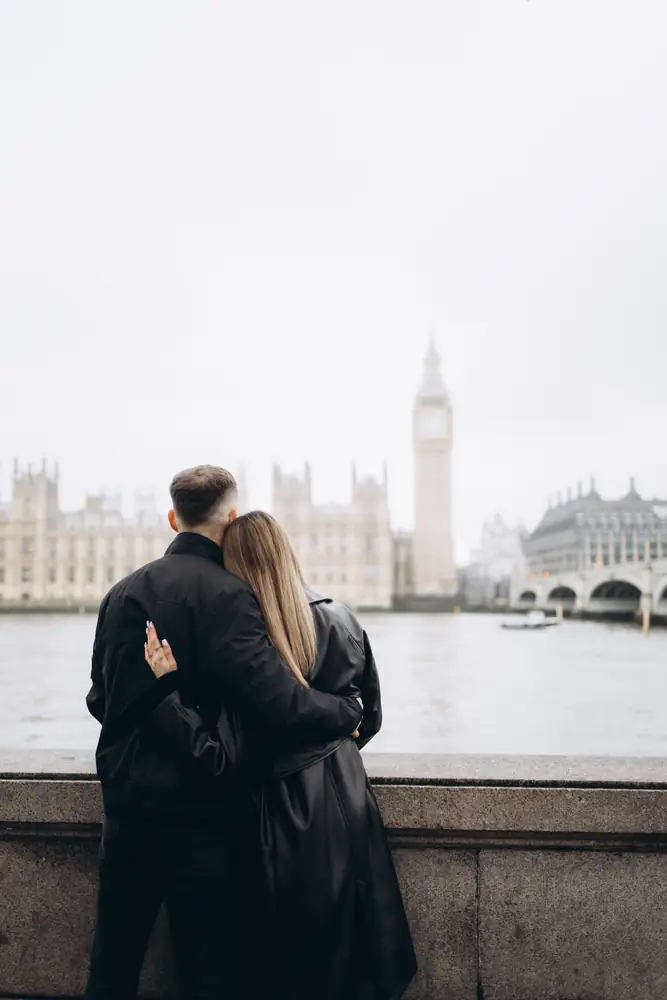 Couple hugging by the Thames river wall, looking across at Big Ben