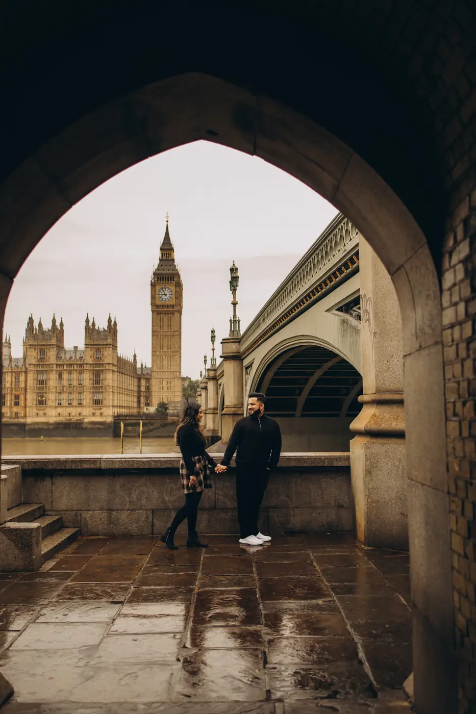 Couple holding hands under the Westminster Bridge arch during a Big Ben photoshoot