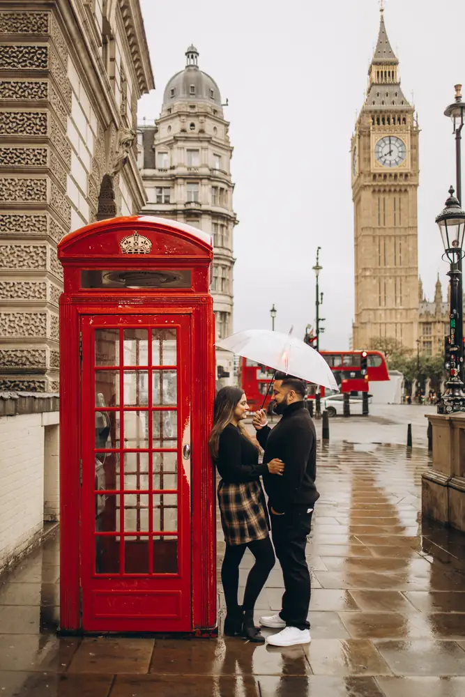 Couple with an umbrella by a red phone box near Big Ben