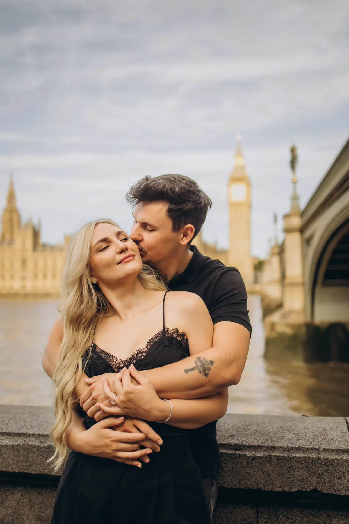 Man hugging his partner from behind by the Thames with Big Ben behind