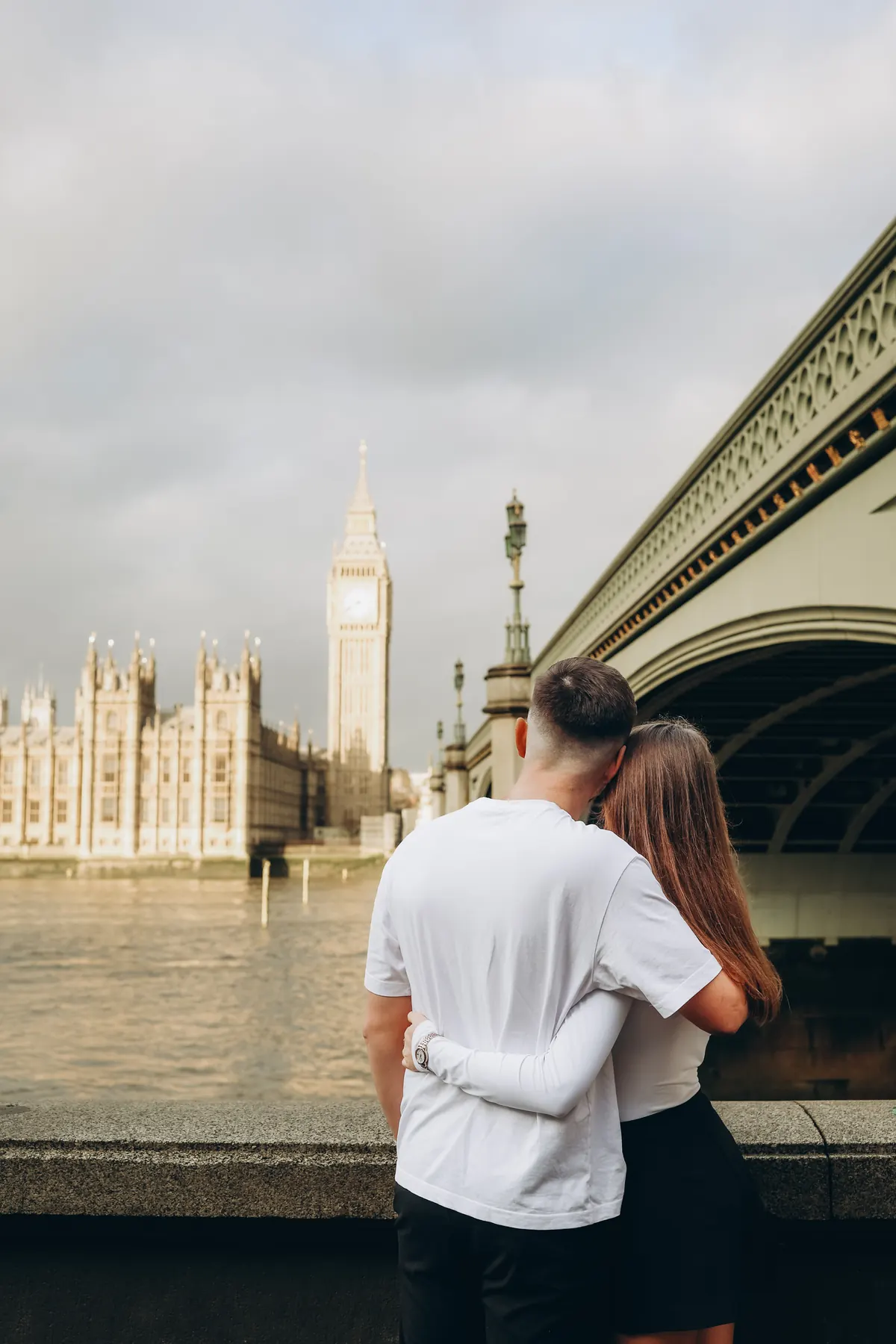 Couple hugging by the Thames, looking at Big Ben under Westminster Bridge