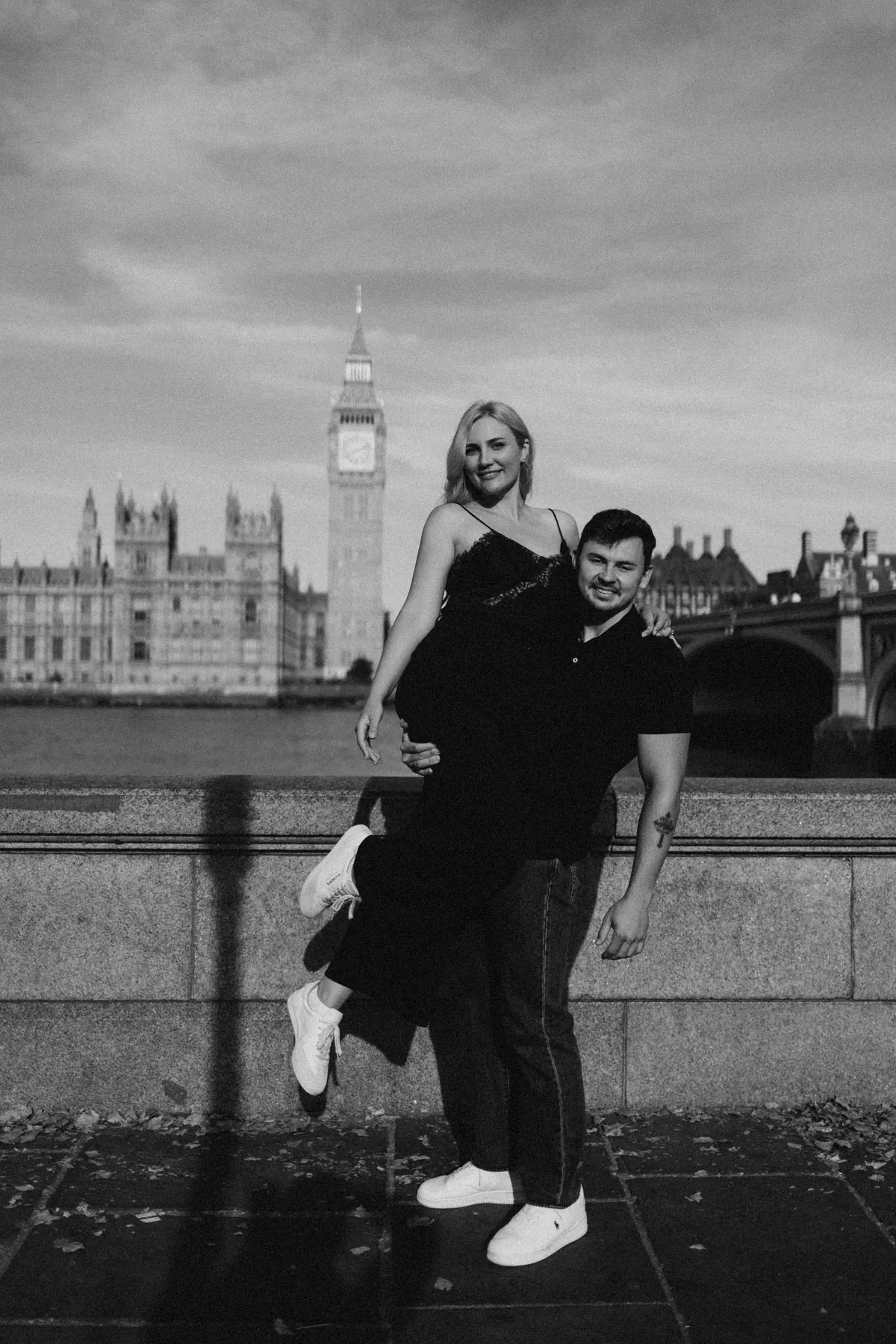 Black and white photo of a man lifting his partner by the Thames with Big Ben behind