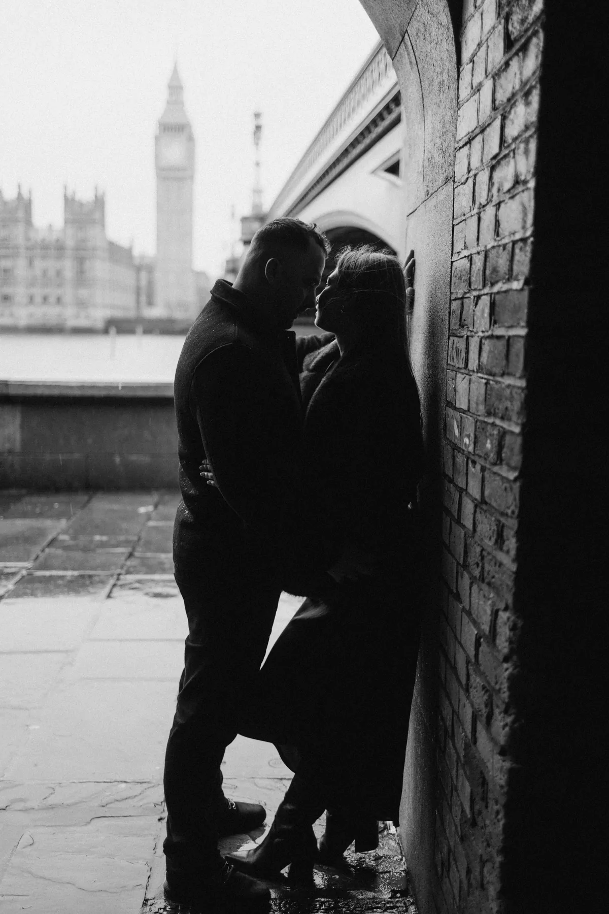 Black and white silhouette of a couple in the arch under Westminster Bridge with Big Ben across the river