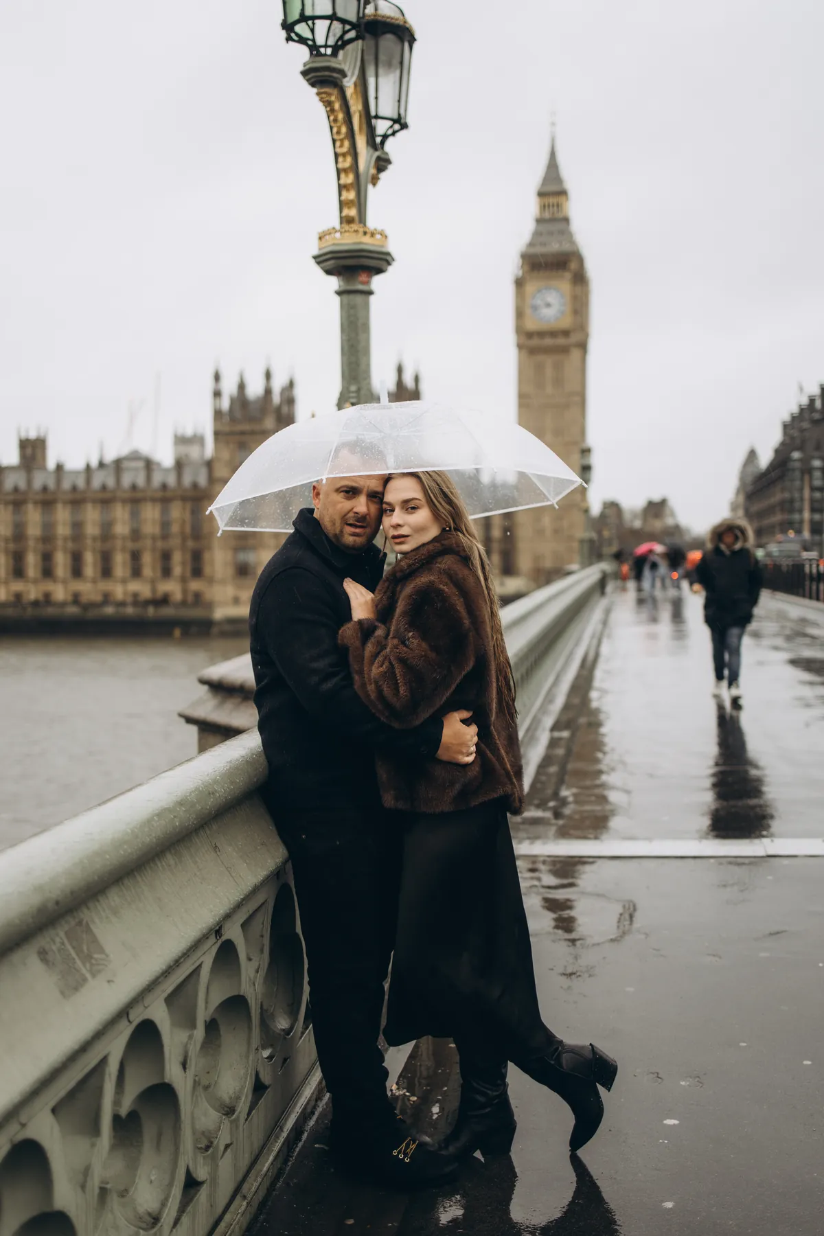 Couple leaning on the Westminster Bridge railing under a clear umbrella with Big Ben behind