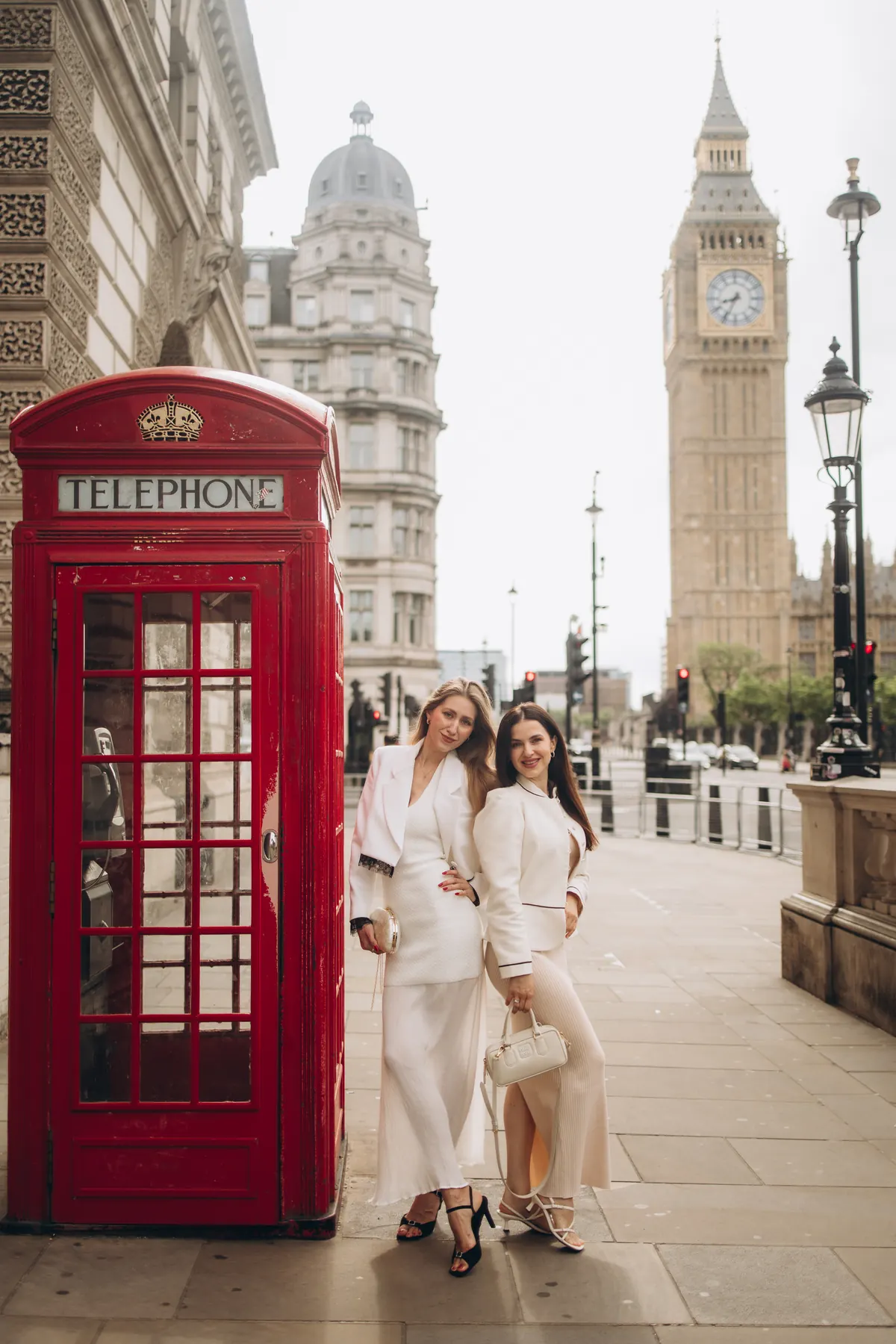 Two friends in white by a red phone box with Big Ben in the background