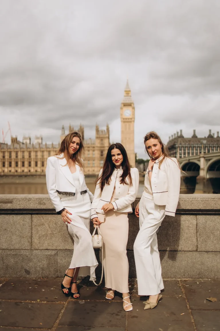 Three friends in white outfits on the river wall with Big Ben and the Houses of Parliament behind