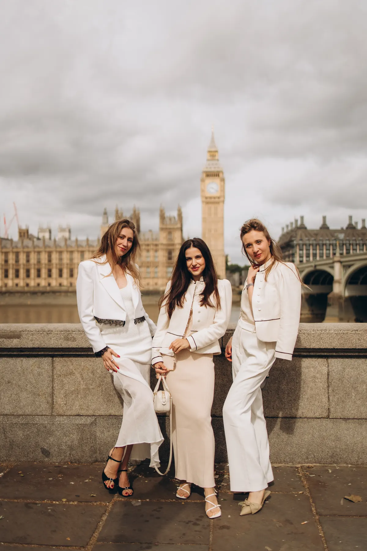Three friends in white outfits on the river wall with Big Ben and the Houses of Parliament behind