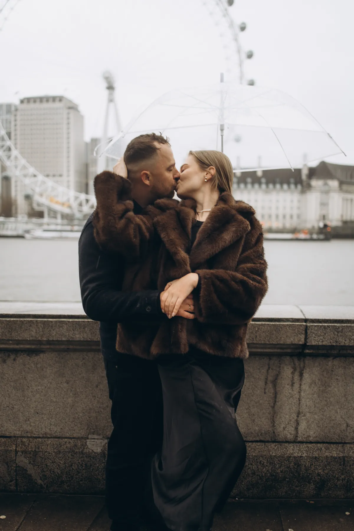 Couple kissing by the river wall with the London Eye across the Thames
