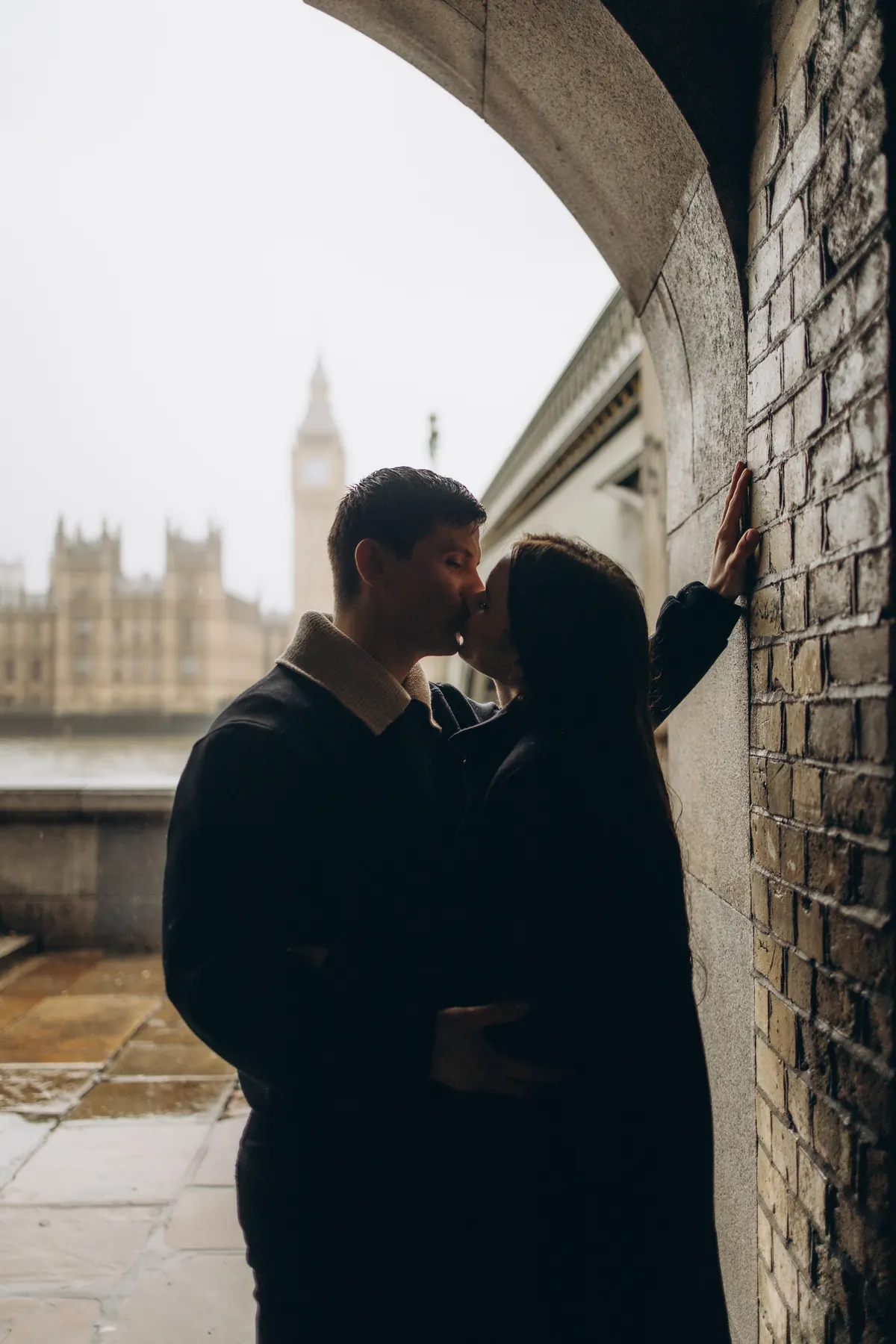 Couple kissing in the shelter of the arch by Westminster Bridge, Big Ben in the rain