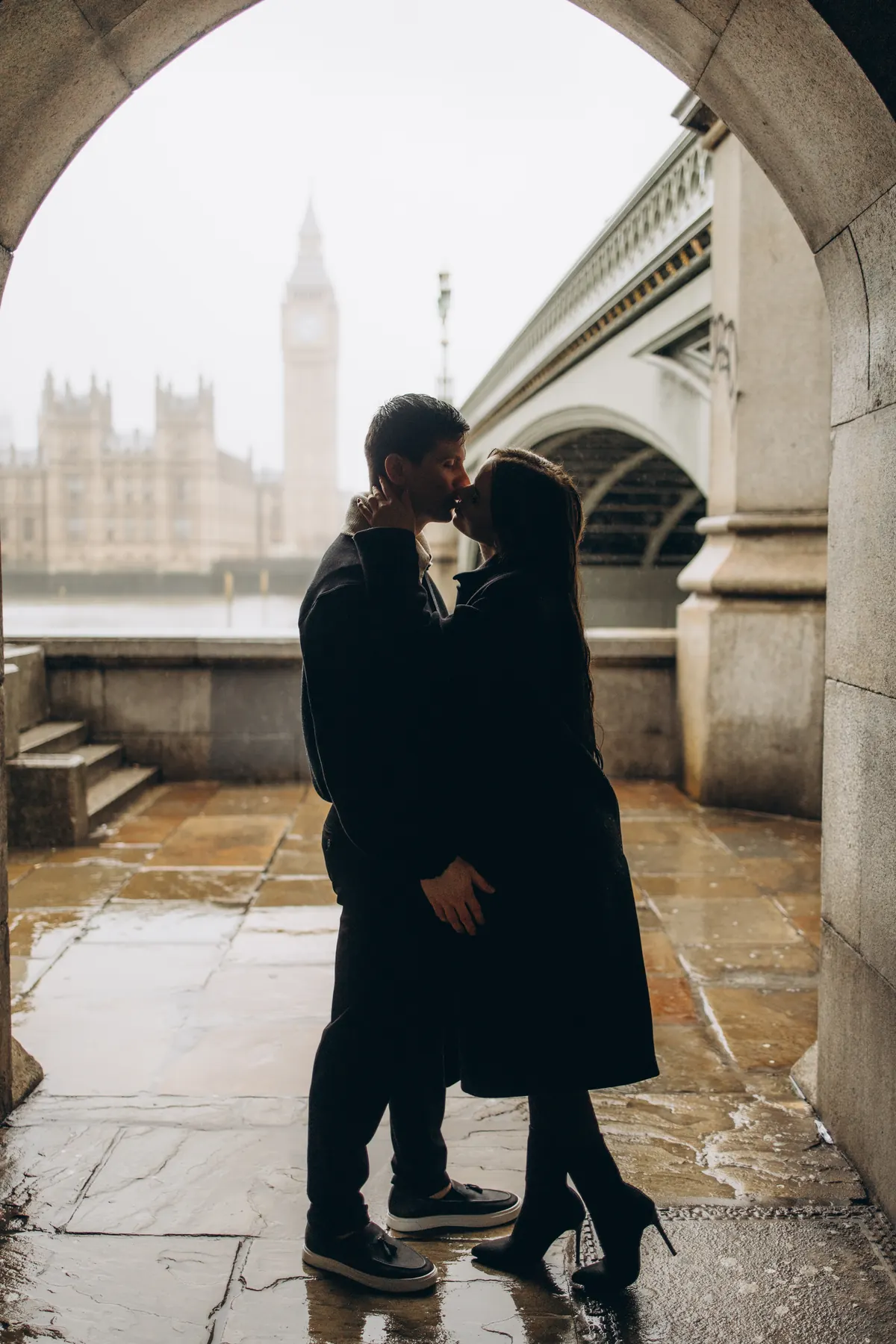 Silhouette of a couple kissing in the arch facing Big Ben on a rainy day