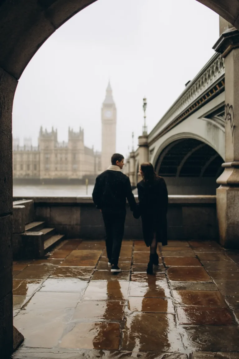 Couple walking hand in hand through the arch towards Big Ben on wet paving