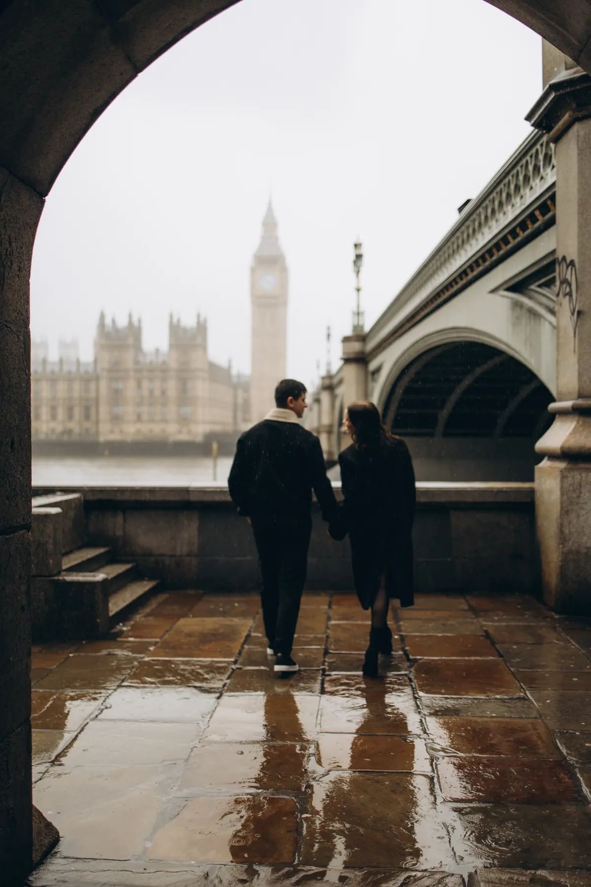 Couple walking hand in hand through the arch towards Big Ben on wet paving
