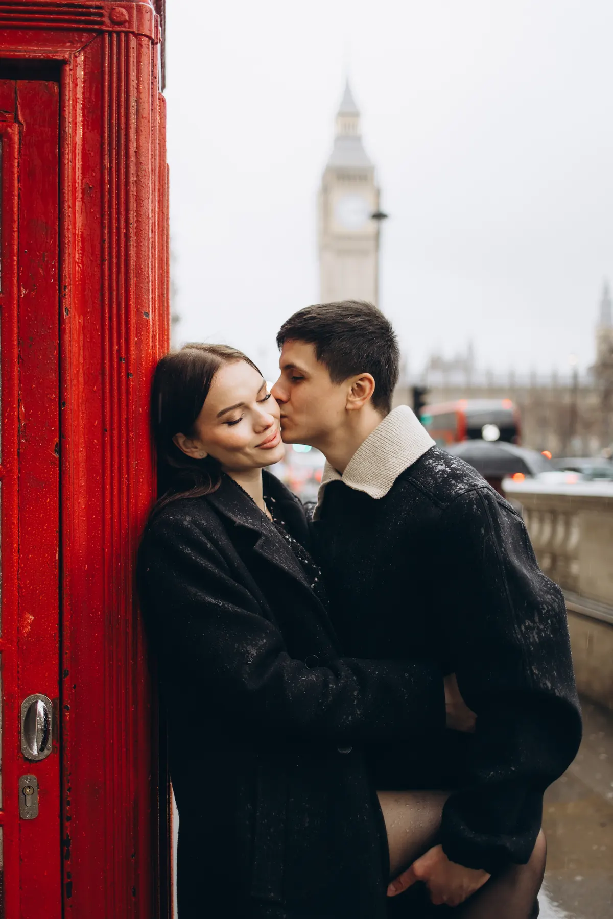 Kiss on the cheek against a wet red phone box with Big Ben in the rain