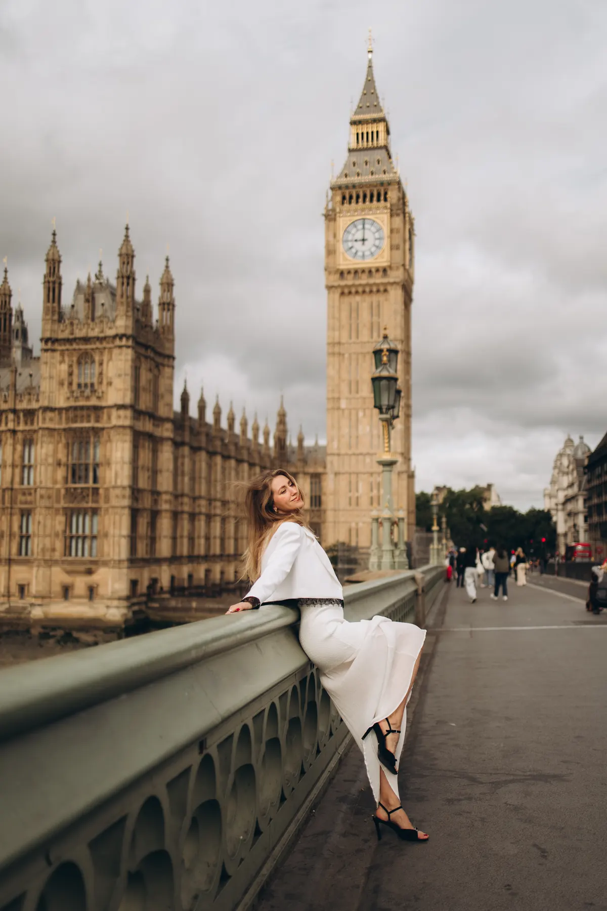Woman in a white jacket and long skirt leaning on Westminster Bridge by Big Ben