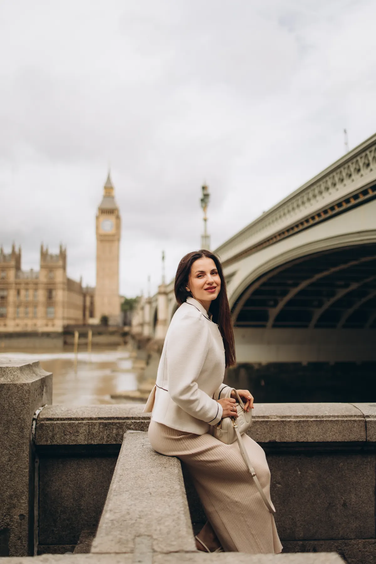 Woman sitting on the wall beside the Westminster Bridge arch with Big Ben behind