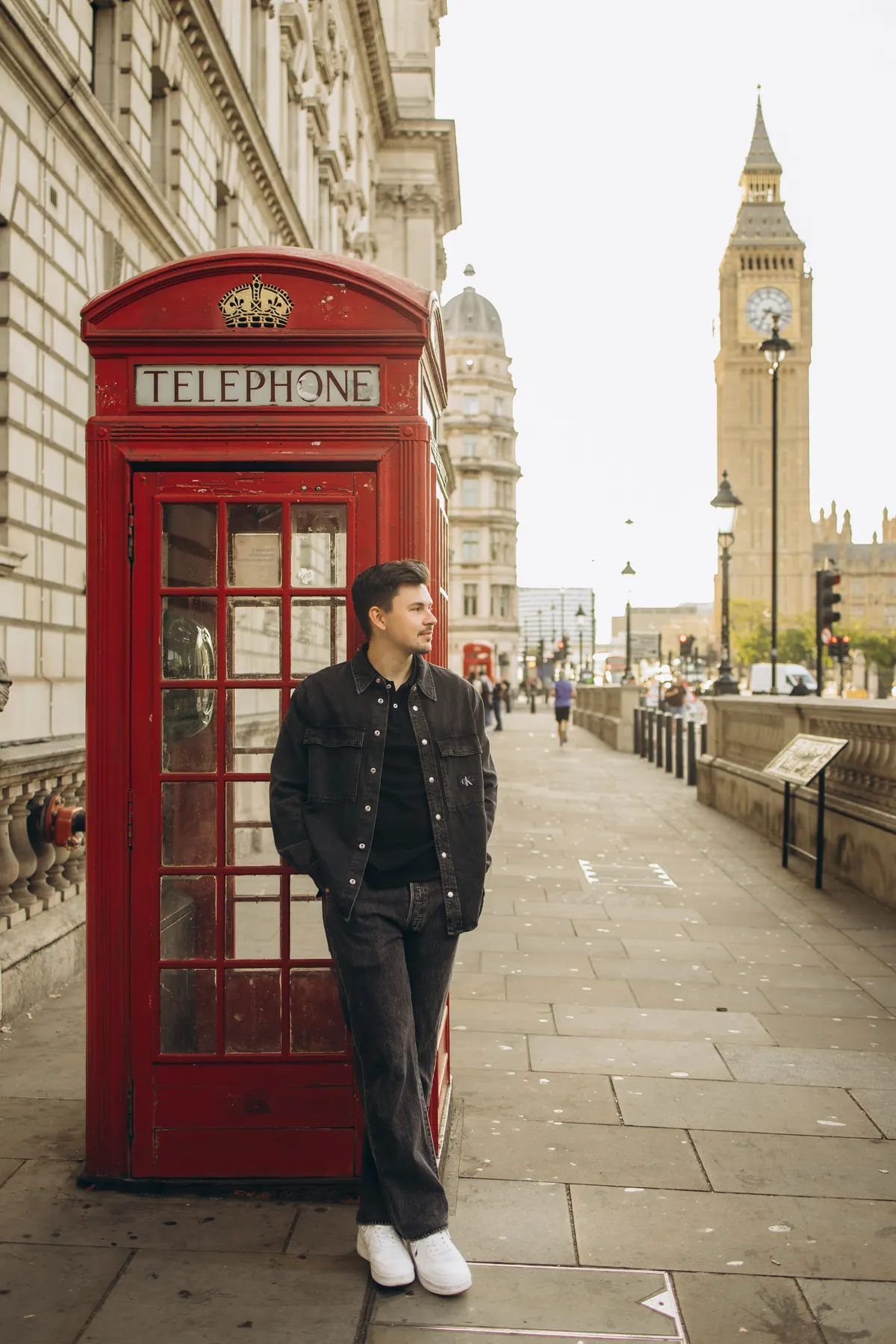 Man in a denim jacket by a red phone box with Big Ben in the distance