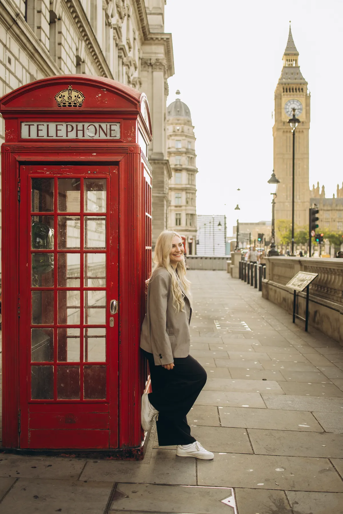 Woman in a grey blazer leaning on a red phone box with Big Ben behind