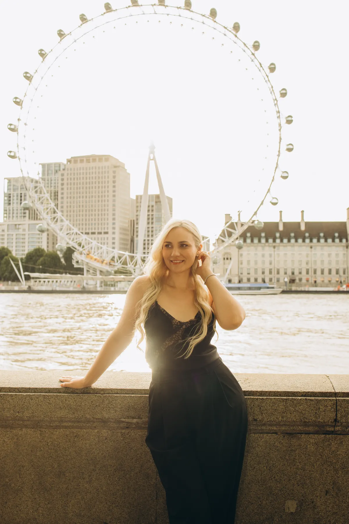 Woman on the Thames wall in sunlight with the London Eye behind