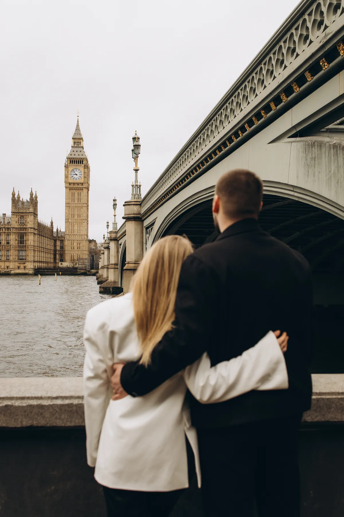 Couple seen from behind with arms around each other, looking across the Thames at Big Ben and Westminster Bridge