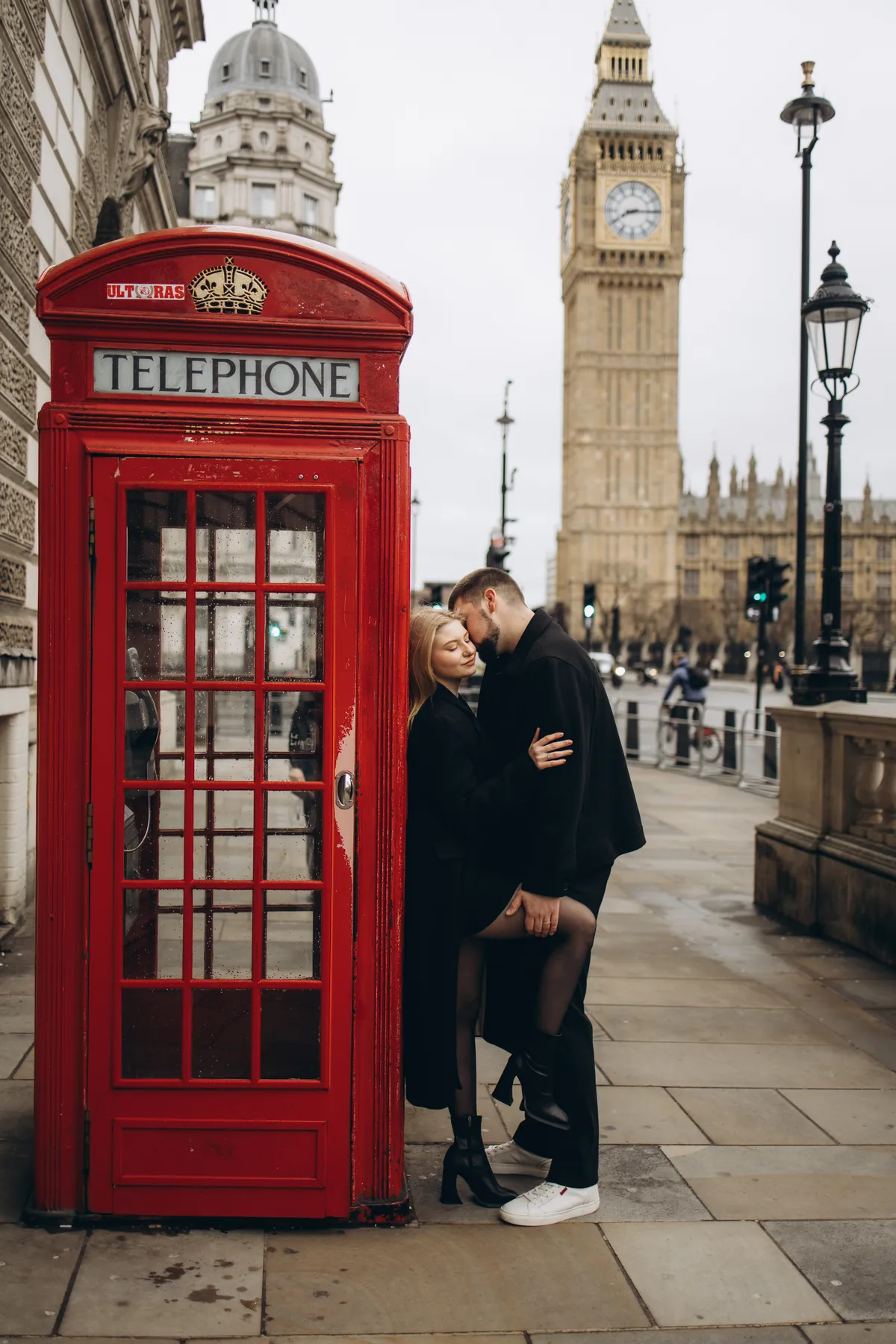 Couple kissing by a red phone box with Big Ben and the Houses of Parliament behind, one heel lifted