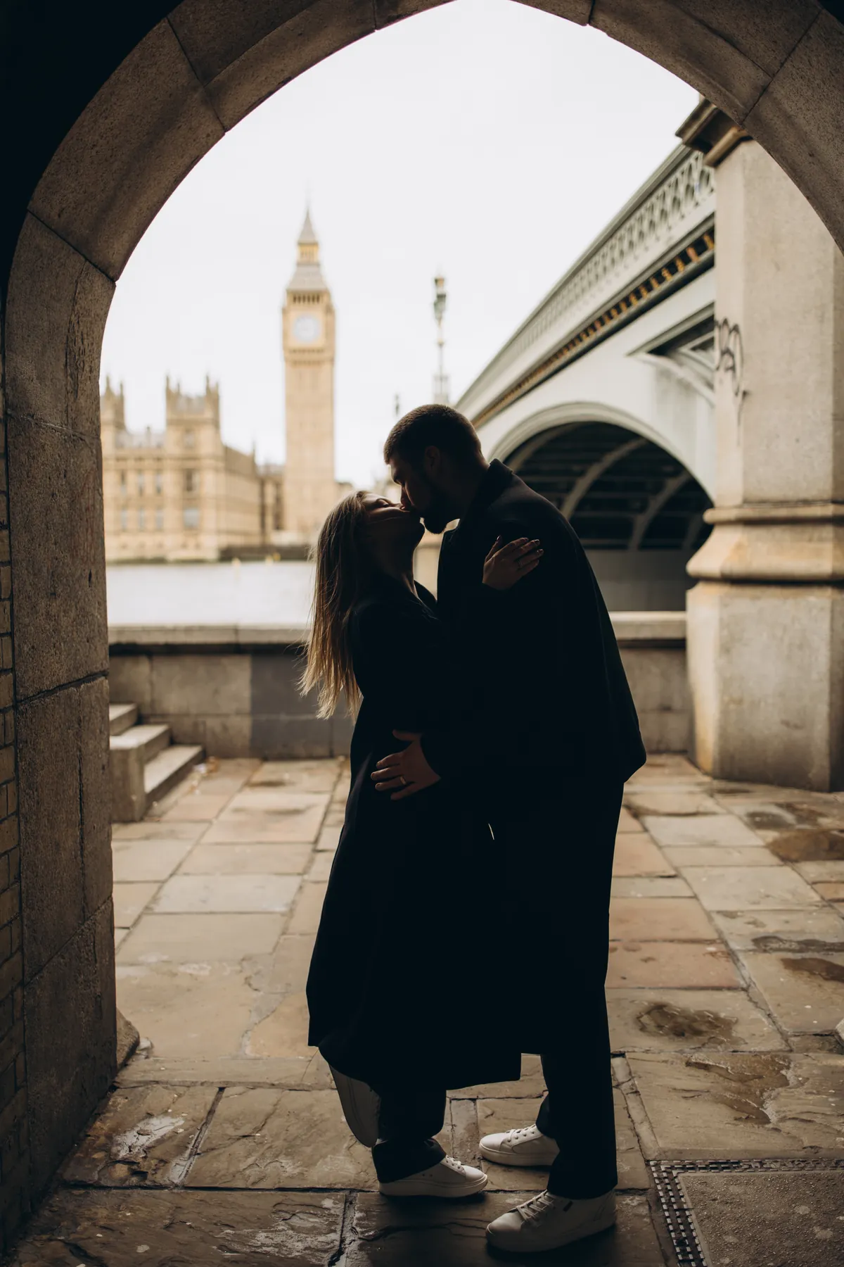Silhouette of a couple kissing in the arch under Westminster Bridge with Big Ben across the river