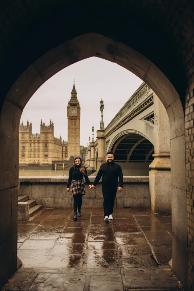 Couple walking hand in hand out of the arch under Westminster Bridge with Big Ben across the river