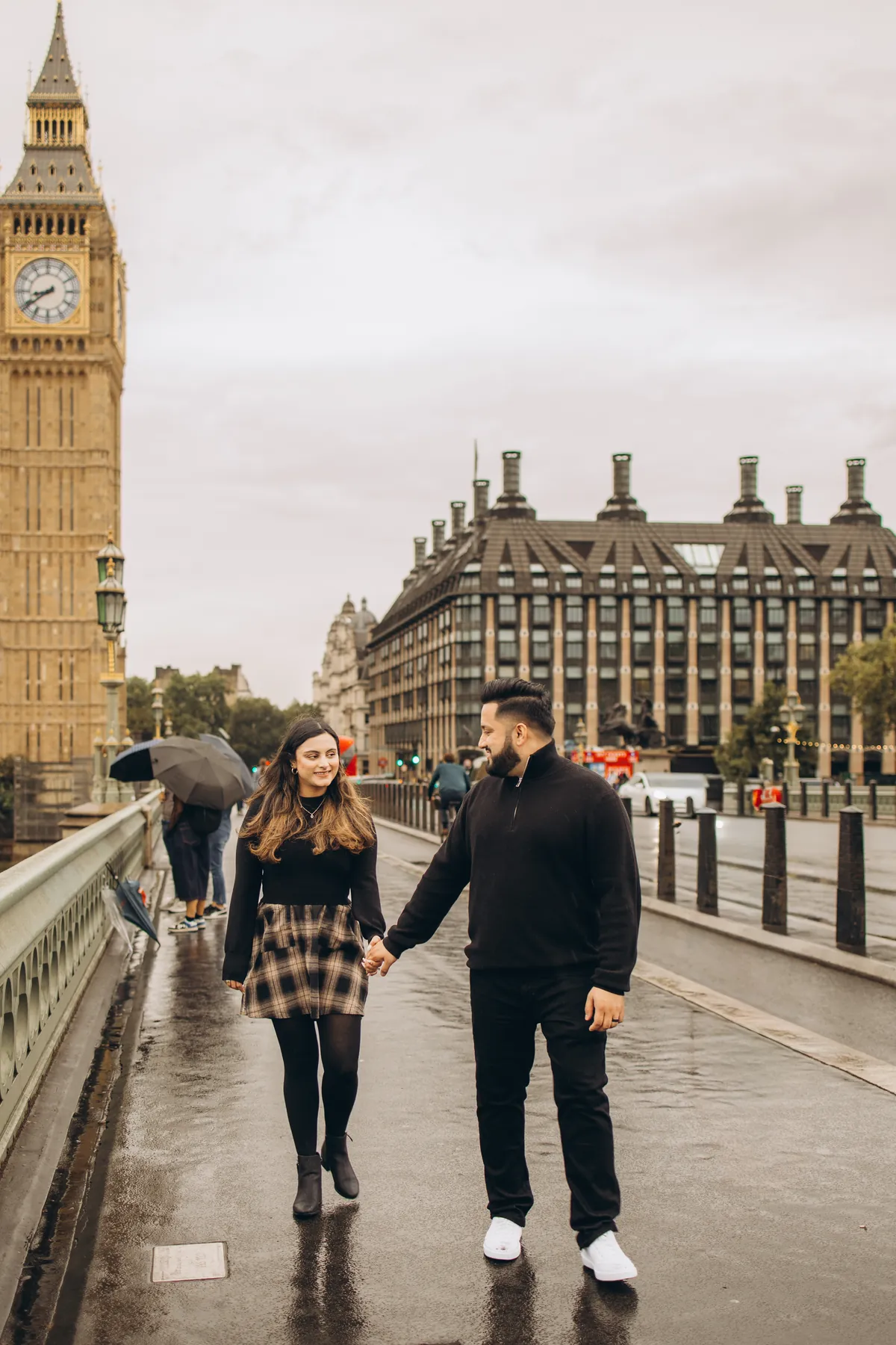 Couple walking hand in hand on a wet Westminster Bridge with Big Ben behind