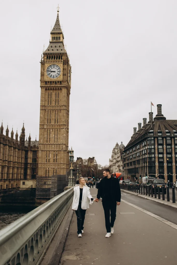 Couple walking hand in hand on Westminster Bridge with Big Ben behind, she in a white blazer