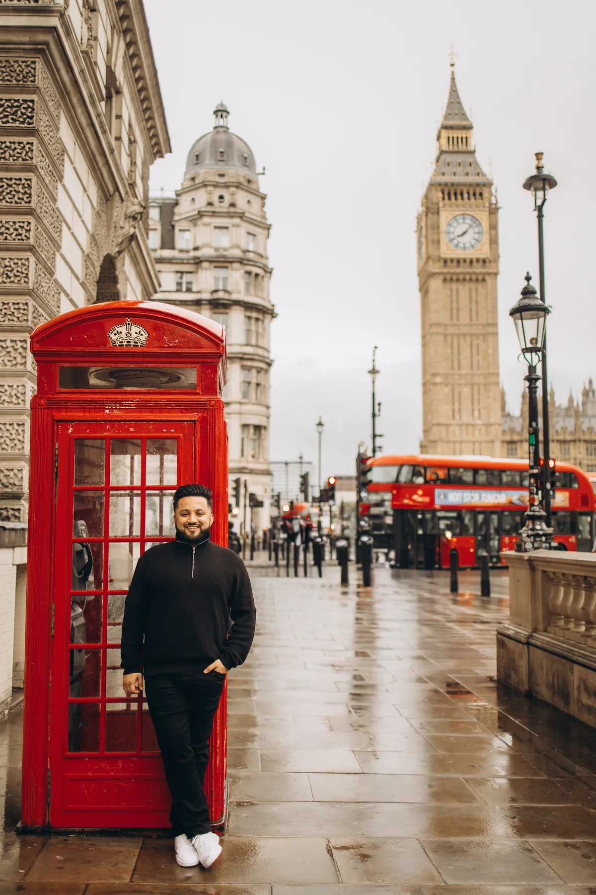 Man leaning on a red phone box with Big Ben and a red double-decker bus behind