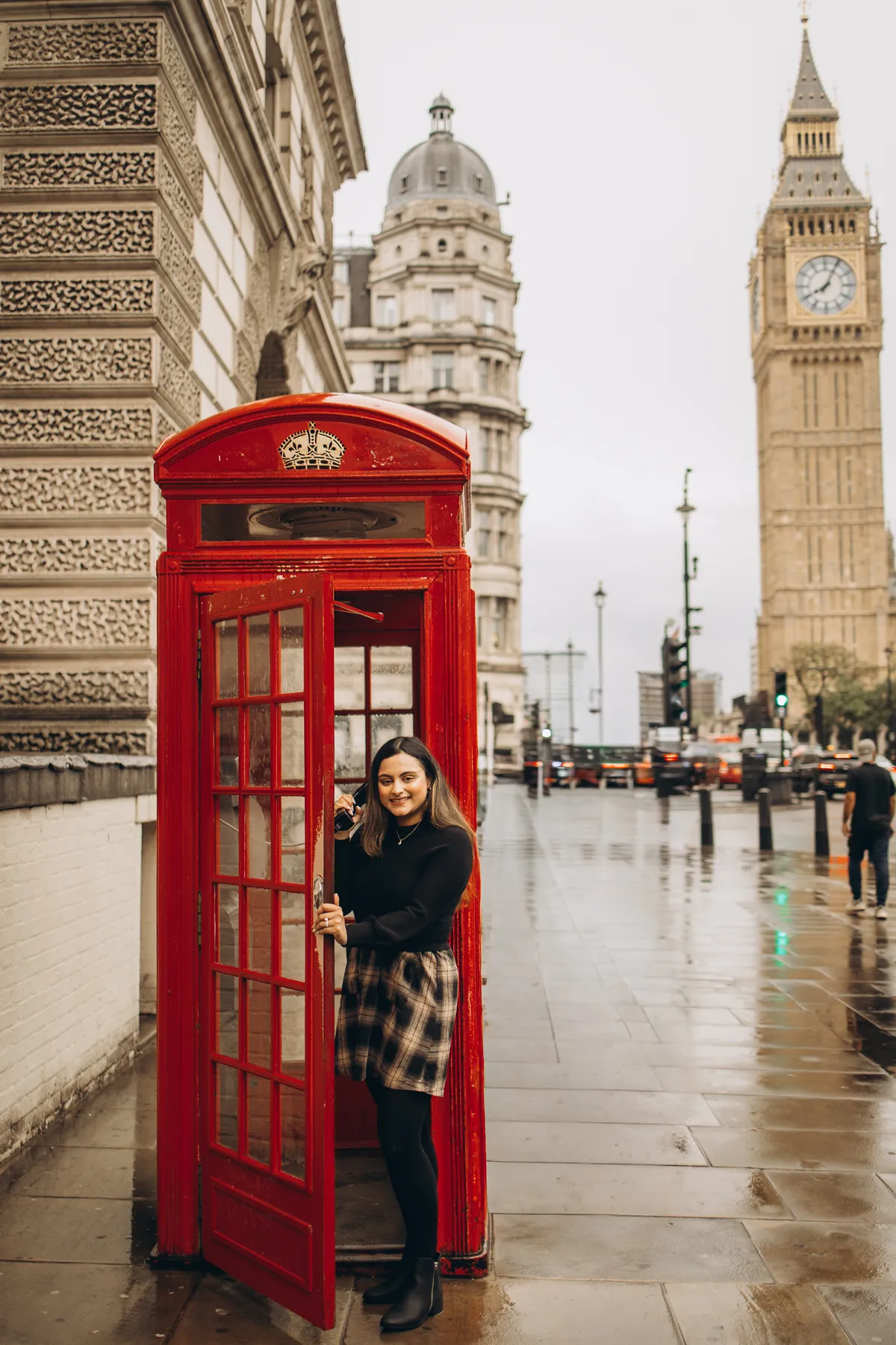 Woman holding the door of a red phone box open, receiver to her ear, Big Ben behind