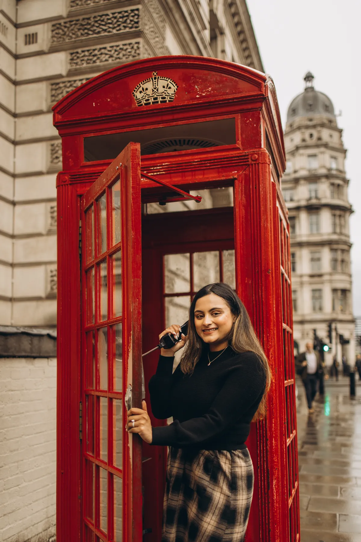 Smiling woman on the phone inside a red phone box near Big Ben