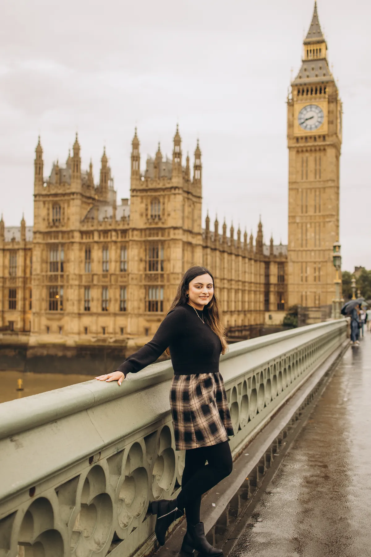 Woman in a plaid skirt leaning on the Westminster Bridge railing with Big Ben behind