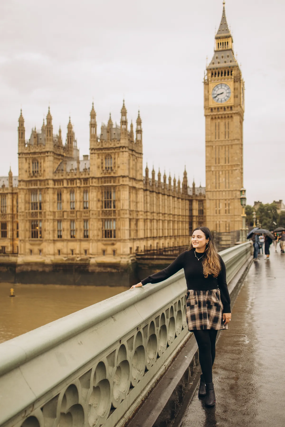 Woman smiling on Westminster Bridge, one hand on the railing, Big Ben and Parliament behind
